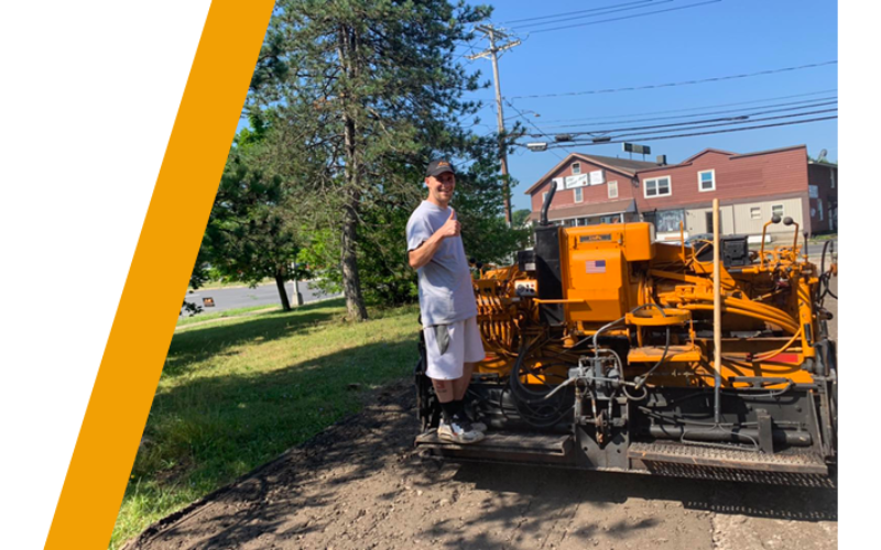 Image of a guy with his thumbs up standing on a construction/paving vehicle